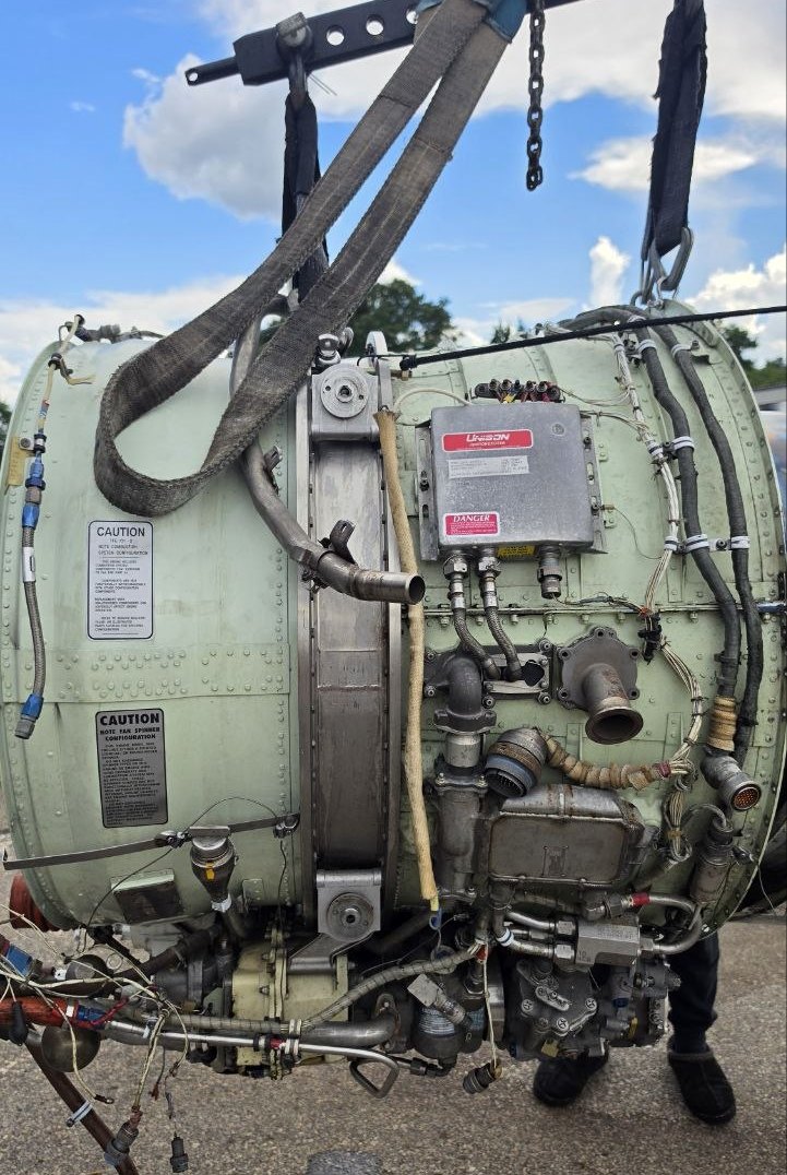 Honeywell TFE731-3 complete turbofan engine on a hoist at Aeromax, Fort Lauderdale — right side view showing accessory gearbox, fuel control unit and ignition exciter